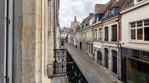 Eine enge Straße mit Häusern an beiden Seiten, im Hintergrund ein Kirchturm und ein Metallbalkon.