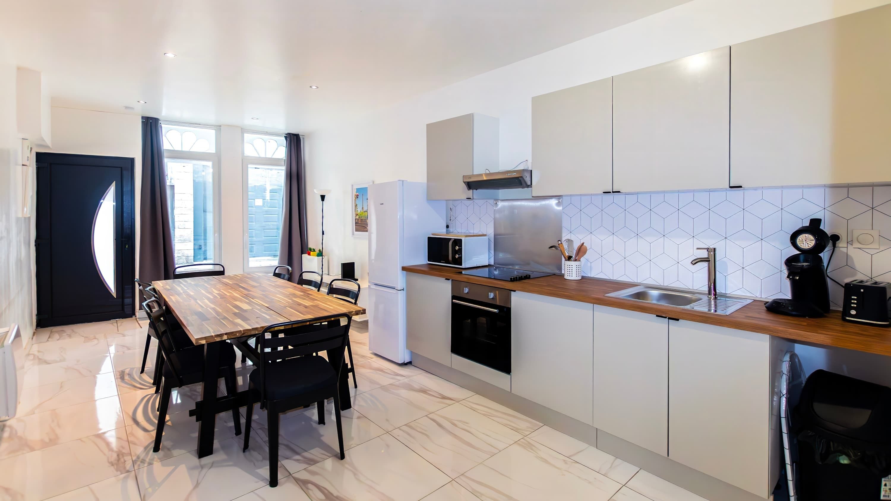 A modern kitchen with a wooden dining table, white cabinets, and a tiled backsplash.