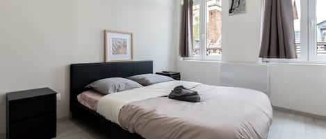 A modern bedroom with a bed, bedside tables, a window with curtains, and a framed picture on the wall.