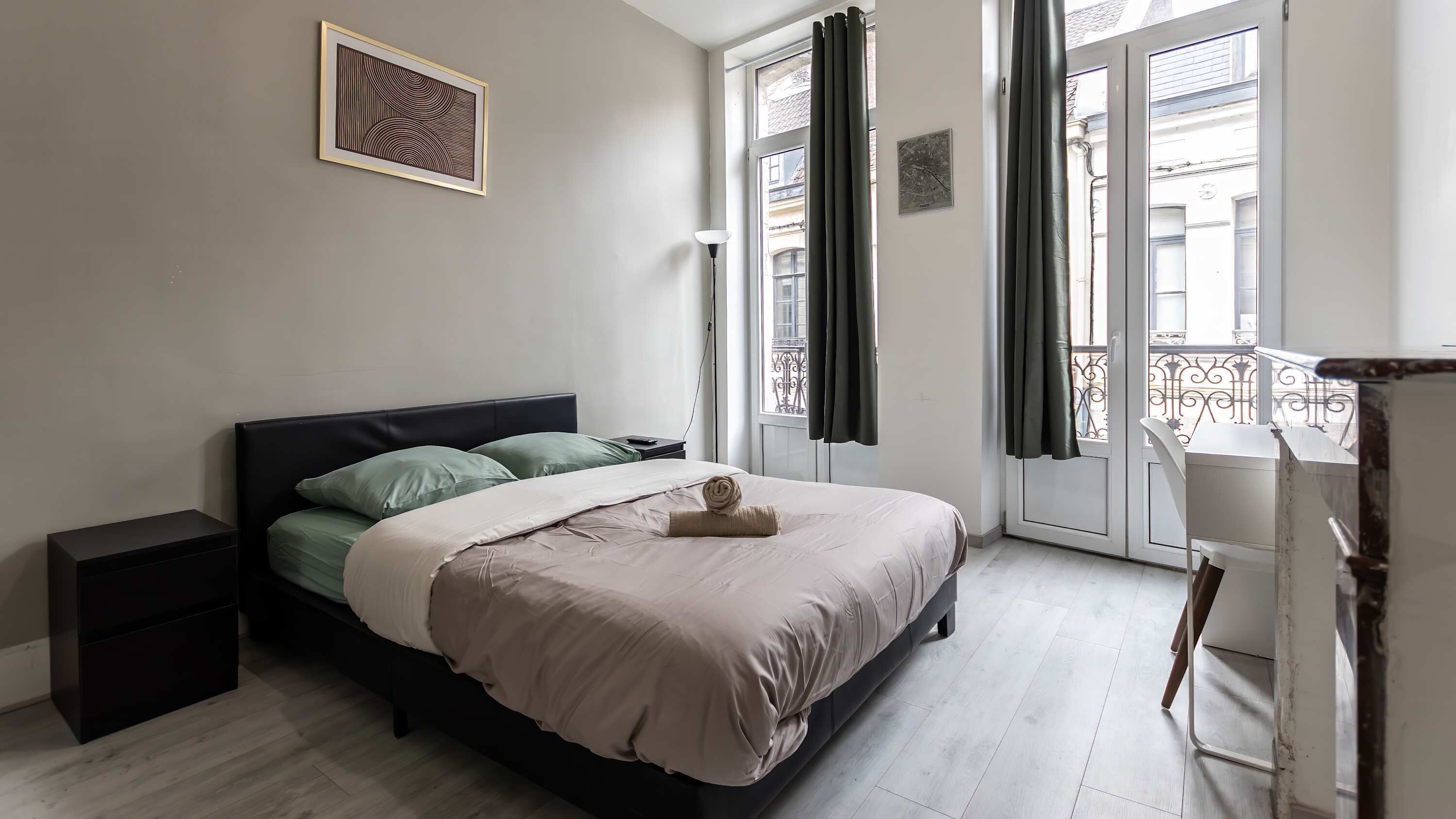 A bedroom with a bed, bedside tables, a window with curtains, a view of the outside, and a painting on the wall.