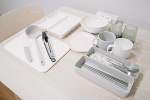 Una mesa bien ordenada con platos, tazones, tazas y cubiertos blancos.