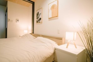 A hotel room with a bed, bedside table, lamp, and wall-mounted artwork. - Seeds Stay Ijiri 2 (Fukuoka)