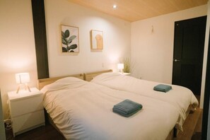 A double bed with two blue towels, a bedside table with a lamp, and two framed pictures on the wall. - Seeds Stay Ijiri 2 (Fukuoka)