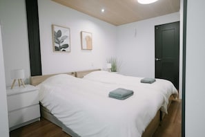 A bedroom with two beds, a bedside table, a lamp, and wall art. - Seeds Stay Ijiri 2 (Fukuoka)