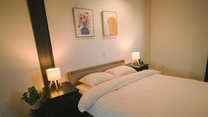 Une chambre à coucher avec un lit, deux tables de chevet, une commode, une lampe et une plante en pot.