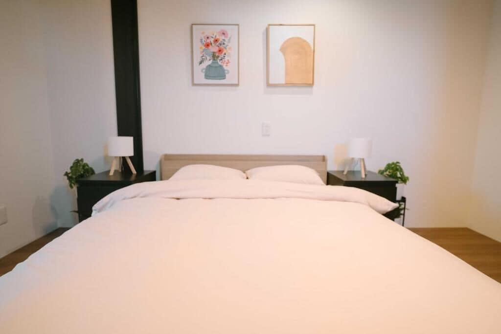 A bedroom with a bed, two bedside tables with lamps, and two wall-mounted artworks.