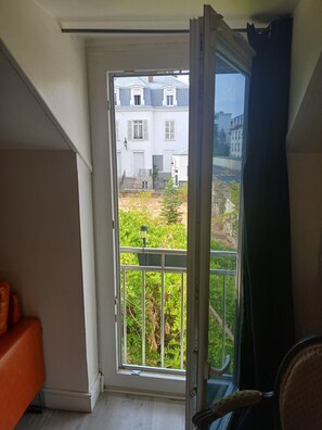 A room with a sliding glass door leading to a balcony with a view of buildings and greenery.