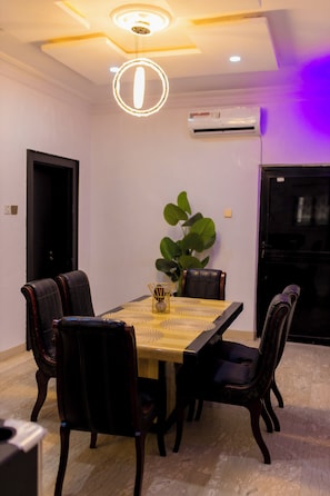 Een eetgedeelte met een rechthoekige tafel, zes stoelen, een plant en een airconditioning.