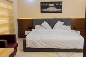 Hotelkamer met een groot bed, hoofdeinde, nachtkastje, stoel en een schilderij aan de muur.