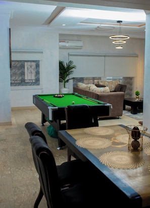 Ein Billardtisch mit Kugeln und Spielstöcken, ein Sofa mit Kissen, ein Blumentopf und ein dekorativer Gegenstand auf dem Boden.