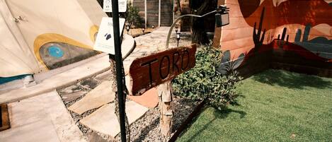 Dans une cour, on peut voir un panneau portant l’inscription « TORO », ainsi qu’une pelouse artificielle, une fresque murale et un élément décoratif aquatique.