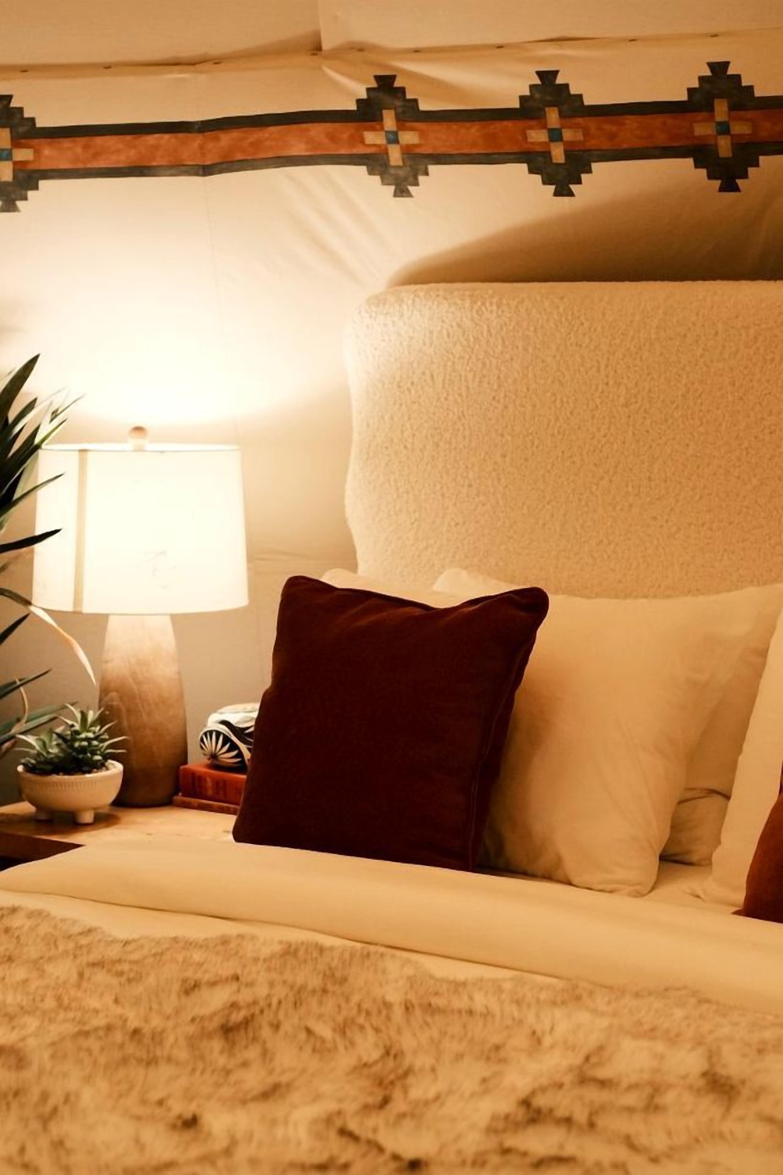 Una cama con una colcha texturizada, un almohadón y un cabecero decorativo.