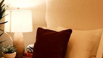 Una cama con una colcha texturizada, un almohadón y un cabecero decorativo.