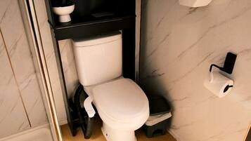 Un baño pequeño con inodoro, un estante con toallas y un dispensador de papel higiénico de pared.