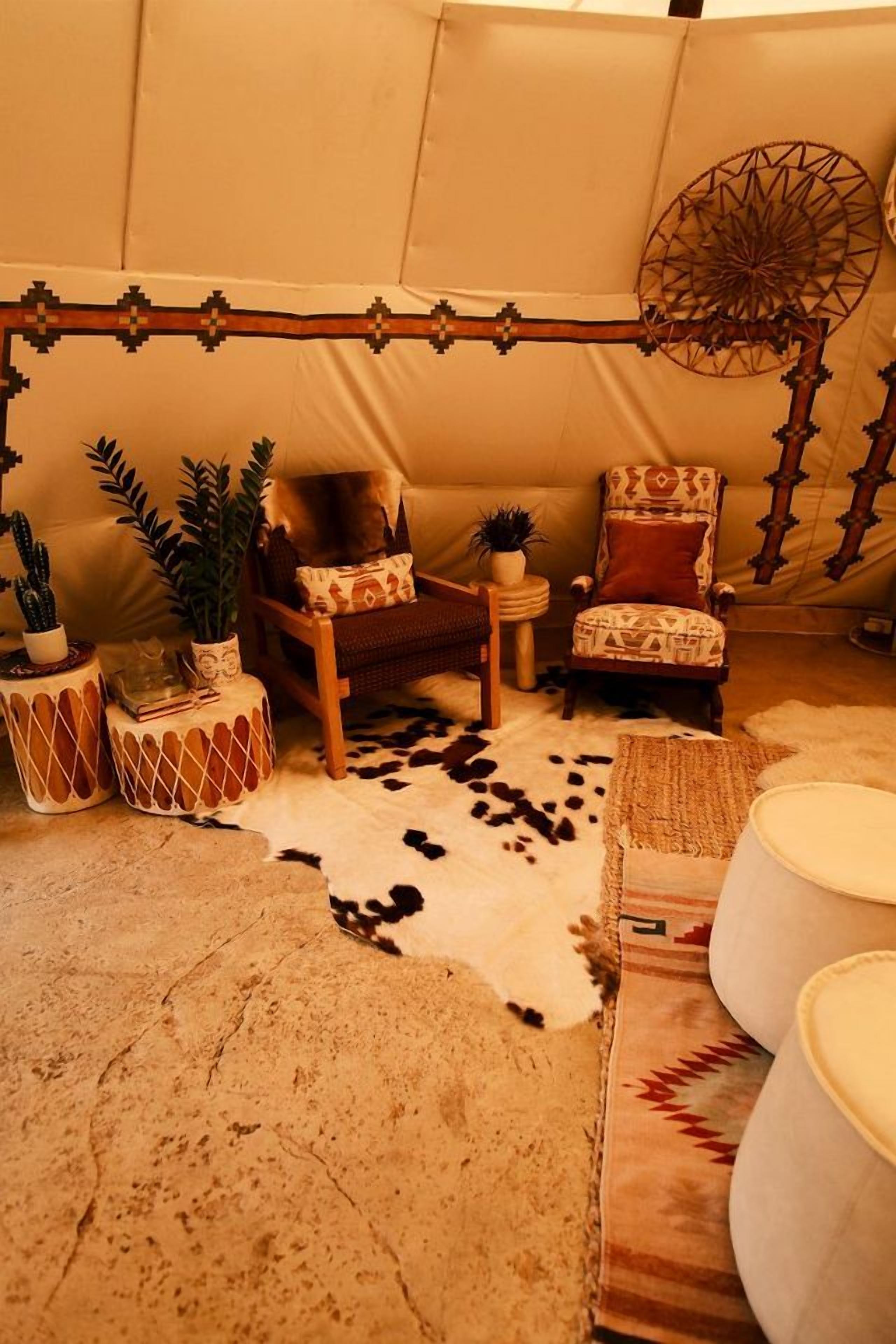 A tent-like room with a patterned wall, two chairs with cushions, a small table, and a cowhide rug.