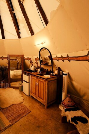 A cozy room with a wooden cabinet, a mirror, a small sink, and a cowhide rug. - Luxurious Tipi with Insulated Comfort Near Ruidoso in Nogal, New Mexico (Nogal)