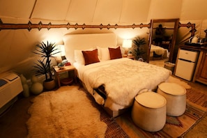 A cozy tent-style bedroom with a bed, bedside tables, a mirror, and a refrigerator.