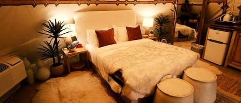 Um quarto aconchegante no estilo de tenda, com cama, mesas de cabeceira, um espelho e um refrigerador.