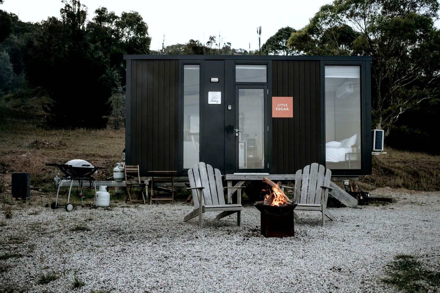 A small cabin with a fire pit, two chairs, and a table.