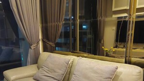 A beige leather sofa with two cushions, positioned in front of a large window with curtains. - Hyde 2BR Luxury Suite Near BTS Nana (Bangkok)