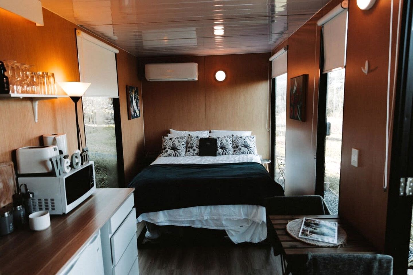 A compact room with a bed, a small table, a microwave, and a window.