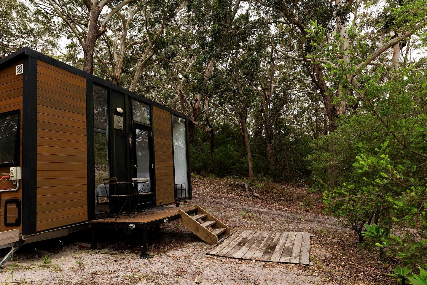 Une petite cabane en bois dotée d’une terrasse et d’un escalier menant à l’entrée.