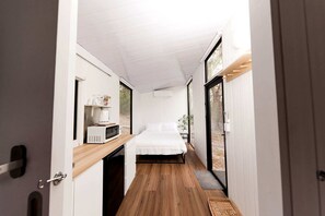 A narrow hallway leading to a bedroom with a bed, a microwave, and a coffee maker on a shelf.