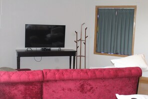 Ein Wohnzimmer mit einem roten Sofa, einem Fernseher auf einem Schrank, einem Fenster mit Vorhängen und einem Kleiderständer.