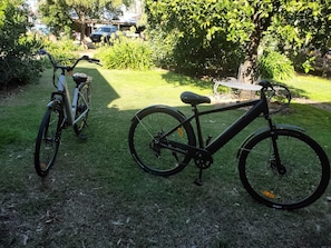 Deux vélos sont garés sur une pelouse, avec des arbres et un bâtiment en arrière-plan.