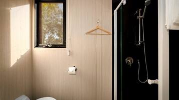 Ein kleines Badezimmer mit Toilette, Papierhalter, einem Fenster und einer Dusche mit Duschhandstück.