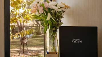 Ein Fenster mit Blick auf Bäume, eine Vase mit Blumen, ein Buch und eine schwarze Box auf einem Holztisch.