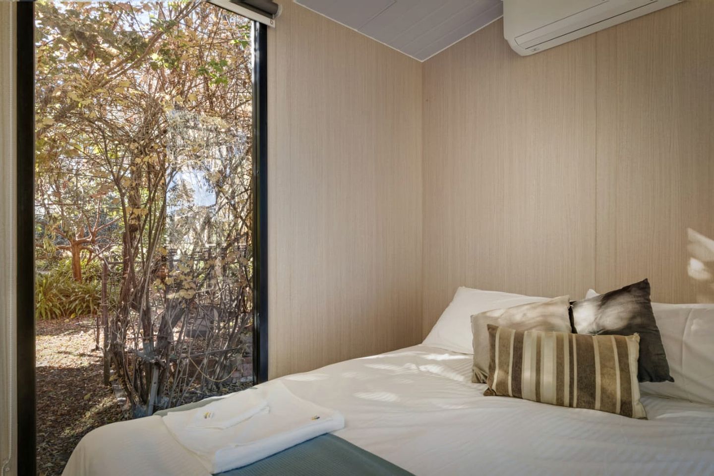 Quarto com cama, almofadas e vista para as árvores pela janela.