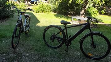 Two bicycles parked on a grassy area with trees and a building in the background.