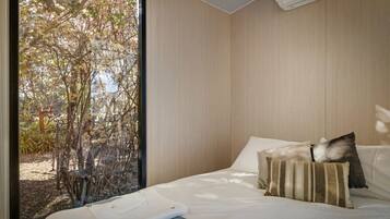 Une chambre à coucher avec un lit, des oreillers et une vue sur les arbres par la fenêtre.