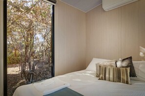 A bedroom with a bed, pillows, and a view of trees through a window.