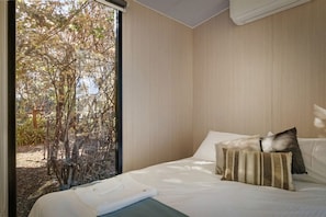Une chambre à coucher avec un lit, des oreillers et une vue sur les arbres par la fenêtre.