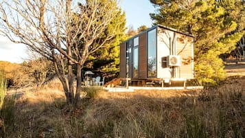 Eine moderne, eingeschossige Hütte mit einem grossen Panoramafenster, umgeben von dichter Vegetation.
