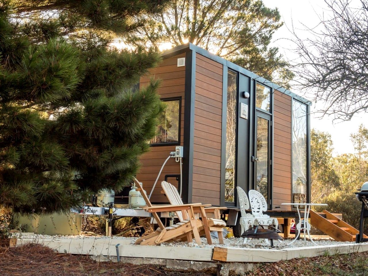 Une cabane moderne avec une façade en bois, de grandes fenêtres et un espace patio doté de meubles d’extérieur.