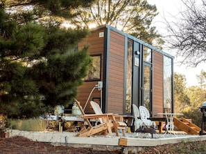 Eine moderne Hütte mit Holzfassade, großen Fenstern und einer Terrasse mit Sitzgelegenheit.
