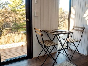 A room with a wooden table and chairs, a window with a view of trees and a deck outside.