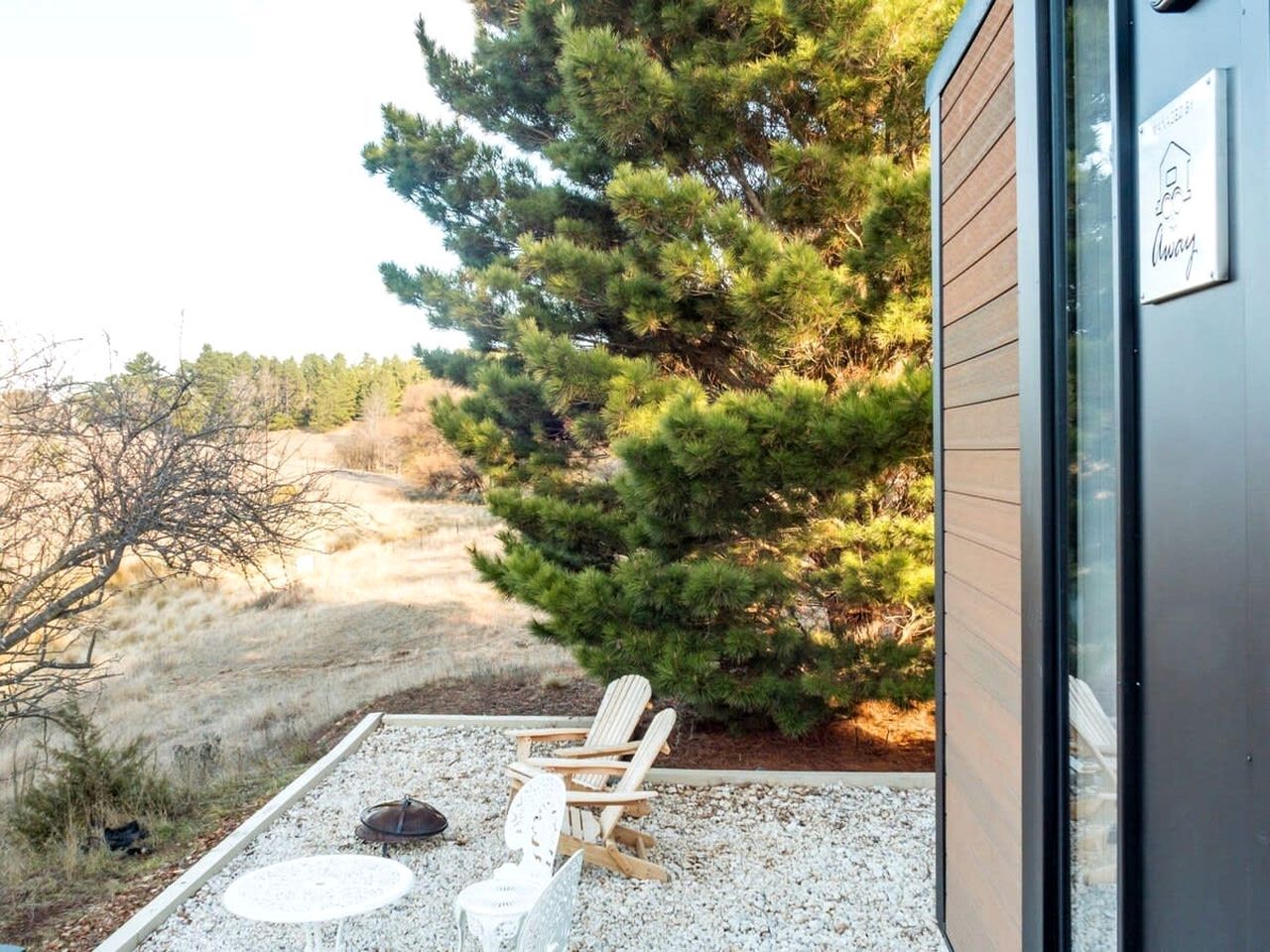Eine Terrasse mit Stuhl und Feuerstelle, umgeben von Kies und einem kleinen Baum.