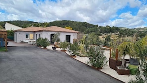 A two-story house with a tiled roof, a paved driveway, and a garden with various plants and a cactus. - Separate master bedroom (Bandol)