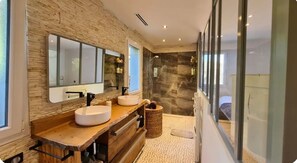 Ein modernes Badezimmer mit Steinwand, großem Spiegel, zwei Waschbecken und einer Duschkabine.