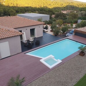 Ein modernes Haus mit Pool, Gartenmöbeln und Blick auf einen bewaldeten Hügel.