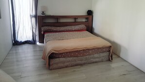 A bedroom with a wooden headboard, a bed with a patterned bedspread, a bedside table with a lamp, and a window with curtains. - Separate master bedroom (Bandol)