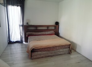Ein Schlafzimmer mit einem Holz-Kopfteil, einem Bett mit einem gemusterten Bettbezug, einem Nachttisch mit einer Lampe und einem Fenster mit Vorhängen.