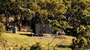Una cabaña apartada con una pequeña terraza, rodeada de un bosque frondoso.