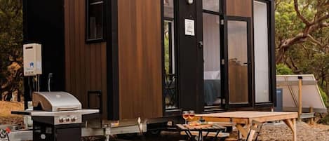 A compact, modern cabin with a built-in grill and a table for outdoor dining.