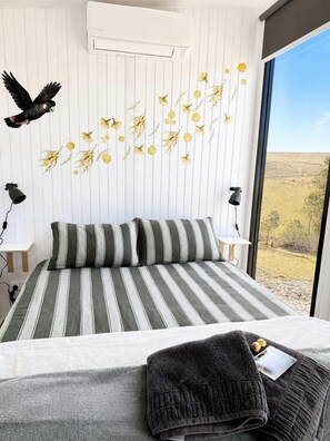 A bedroom with a large bed, a window with a view, and a wall-mounted air conditioner.