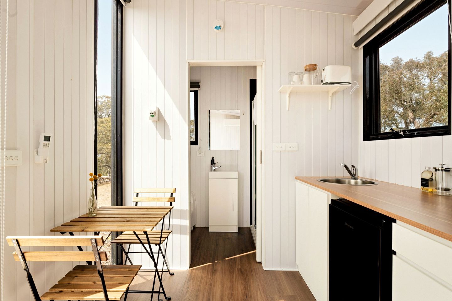 Une cuisine moderne avec des meubles blancs, une table à manger en bois et une fenêtre donnant sur les arbres.